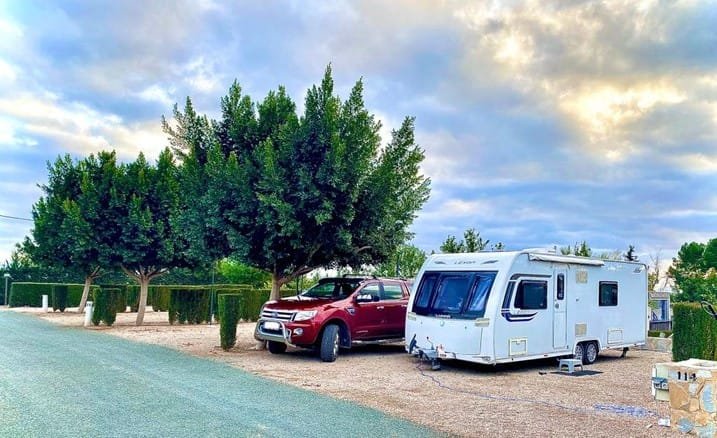 Caravana estacionada en camping en Murcia junto a coche rojo