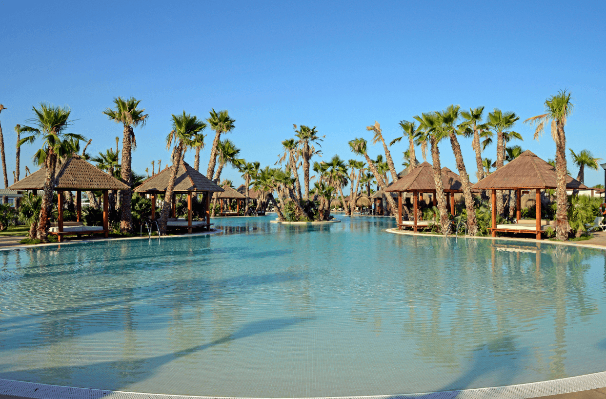 Gran piscina tipo laguna con palmeras y pérgolas en camping en Alicante