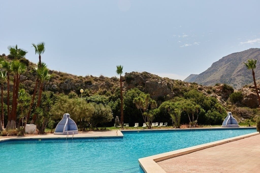 Piscina al aire libre rodeada de montañas y palmeras en camping de Murcia y alrededores