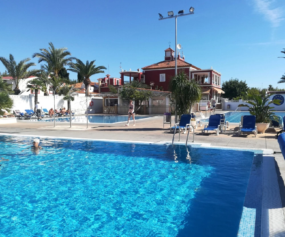 Piscina y zona de descanso en Camping Bahía Santa Pola Alicante con hamacas y edificio principal