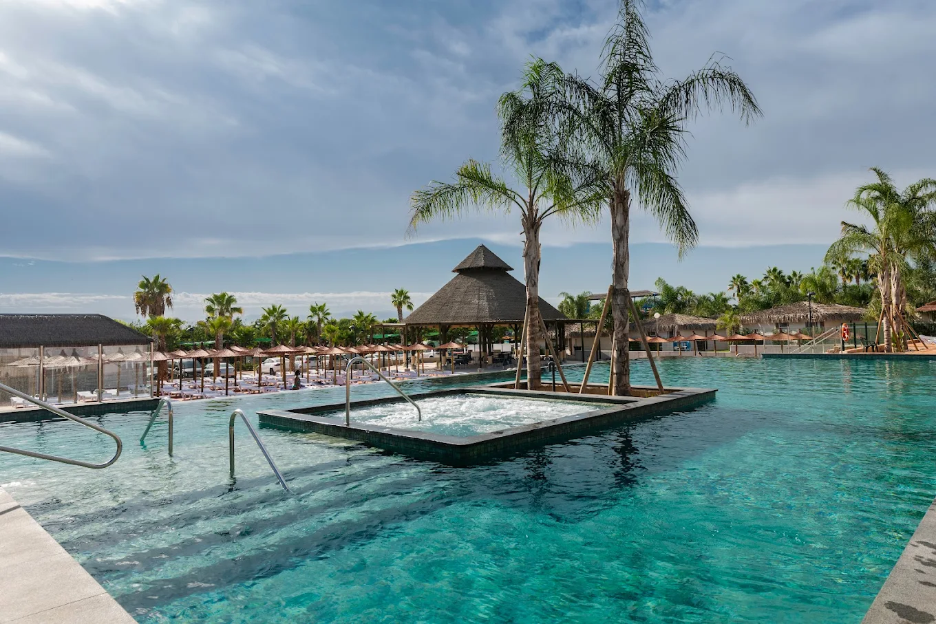 Piscina tropical de camping con palmeras y zona de relax para viajeros en autocaravana