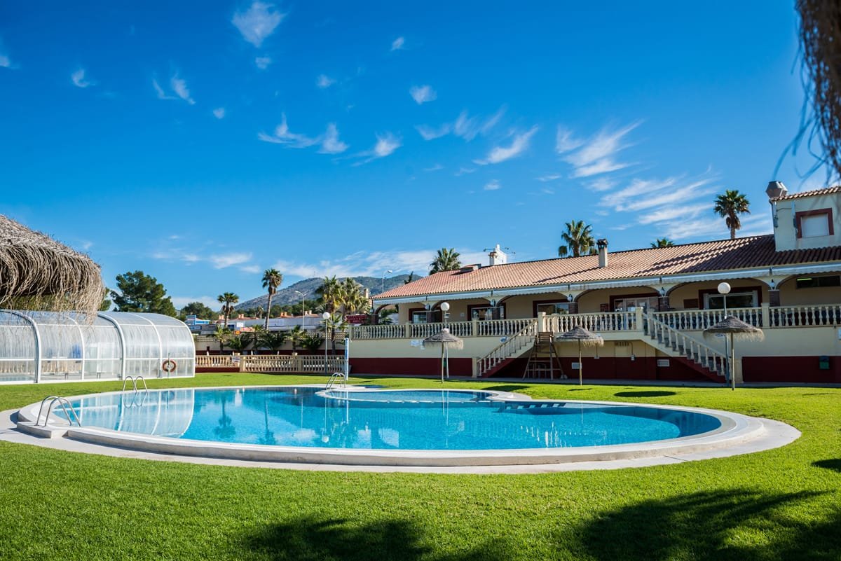 Piscina exterior y edificio principal del Camping Racó en Benidorm Alicante con zona ajardinada