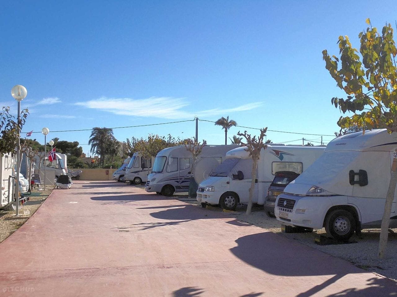 Calle interior del camping con autocaravanas estacionadas en parcelas delimitadas y zona de tránsito peatonal