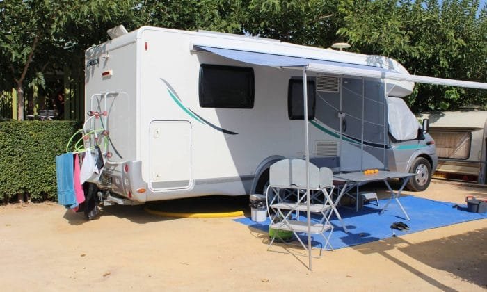 Autocaravana estacionada en camping de Benidorm con toldo abierto, mesa y sillas plegables sobre alfombra exterior en parcela sombreada