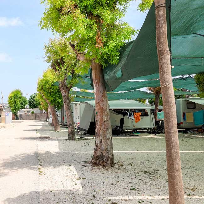 Parcelas amplias para caravanas y autocaravanas con sombra natural de arbolado y mallas protectoras, suelo de grava y acceso cómodo para estacionamiento y estancia tranquila