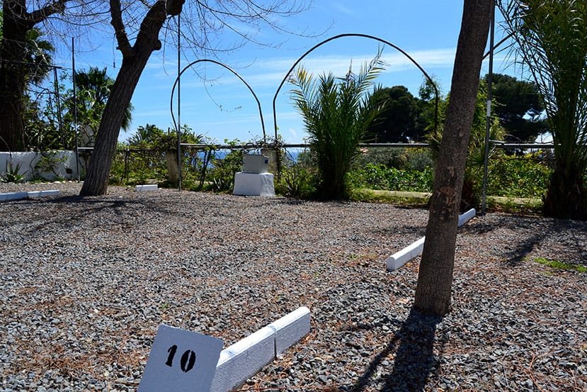 Parcela numerada en camping con superficie de grava, delimitación perimetral y vegetación natural con vista parcial al mar