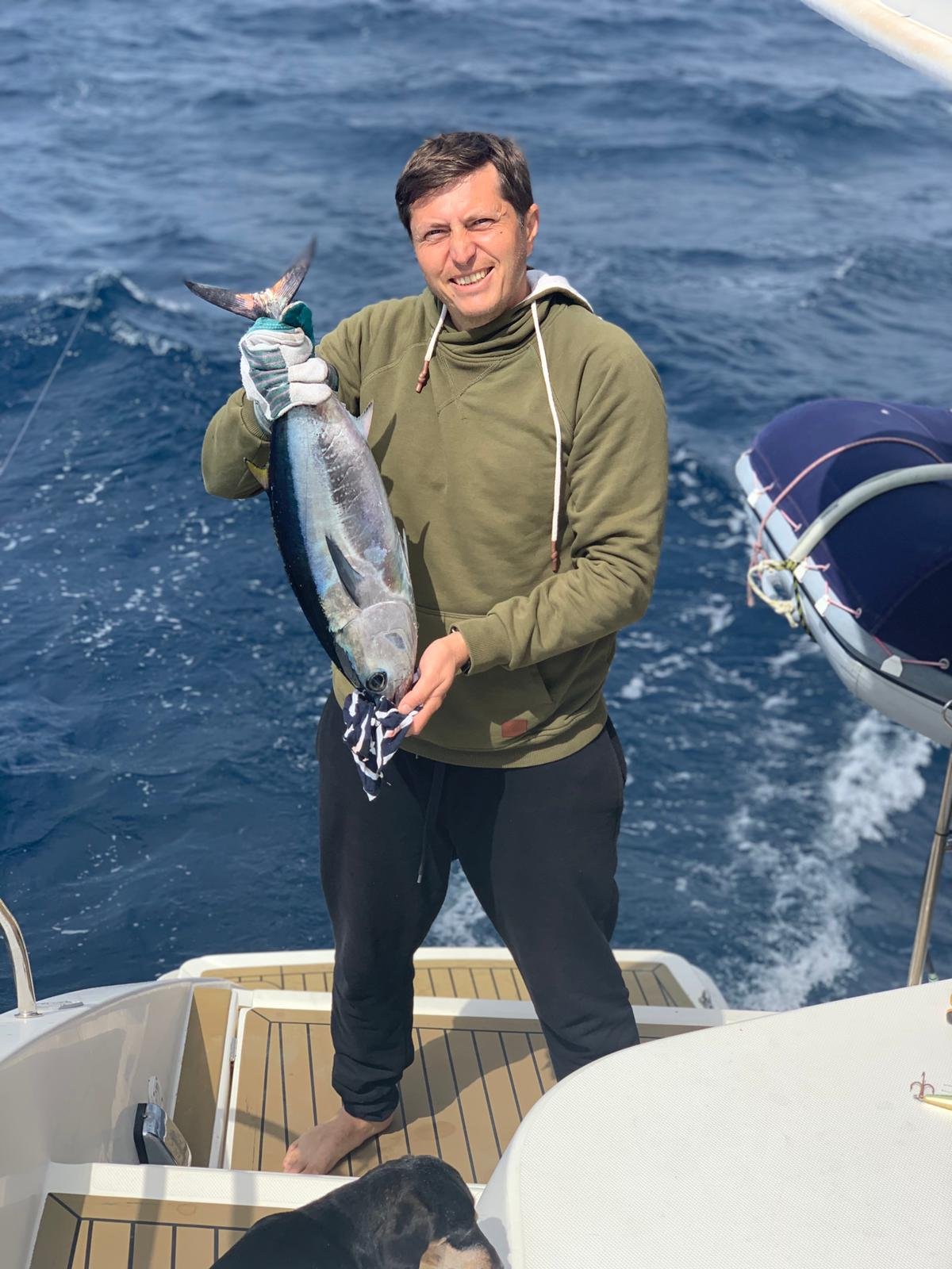 Persona sonriendo en una embarcación mientras sostiene un pez recién capturado en alta mar